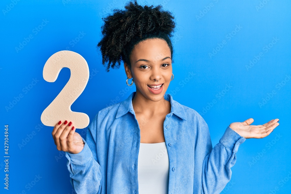 Young african american girl holding number two celebrating achievement with happy smile and winner expression with raised hand Young african american girl holding number two celebrating achievement with happy smile and winner expression with raised hand