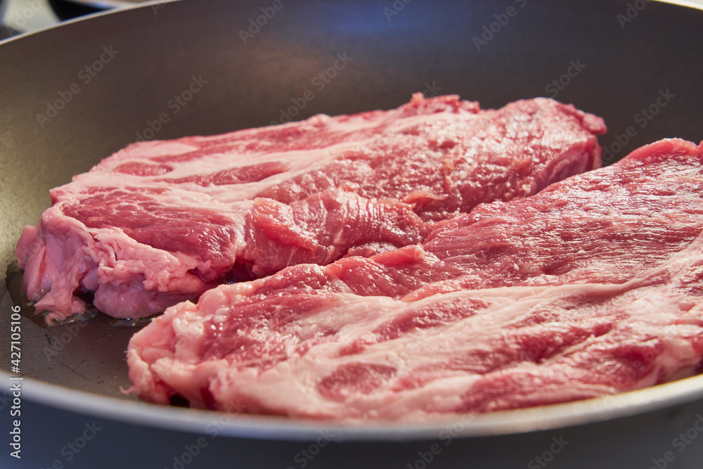 Red pork steaks with a fat layer in a frying pan. Red pork steaks with a fat layer in a frying pan.