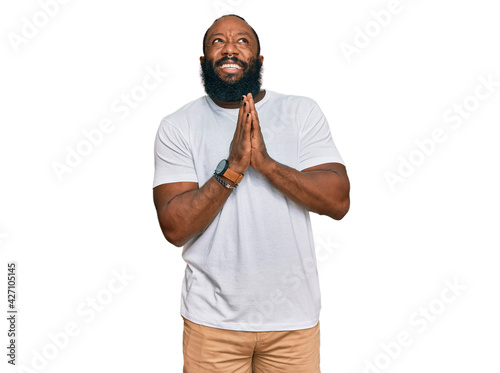 Young african american man wearing casual white tshirt begging and praying with hands together with hope expression on face very emotional and worried. begging.