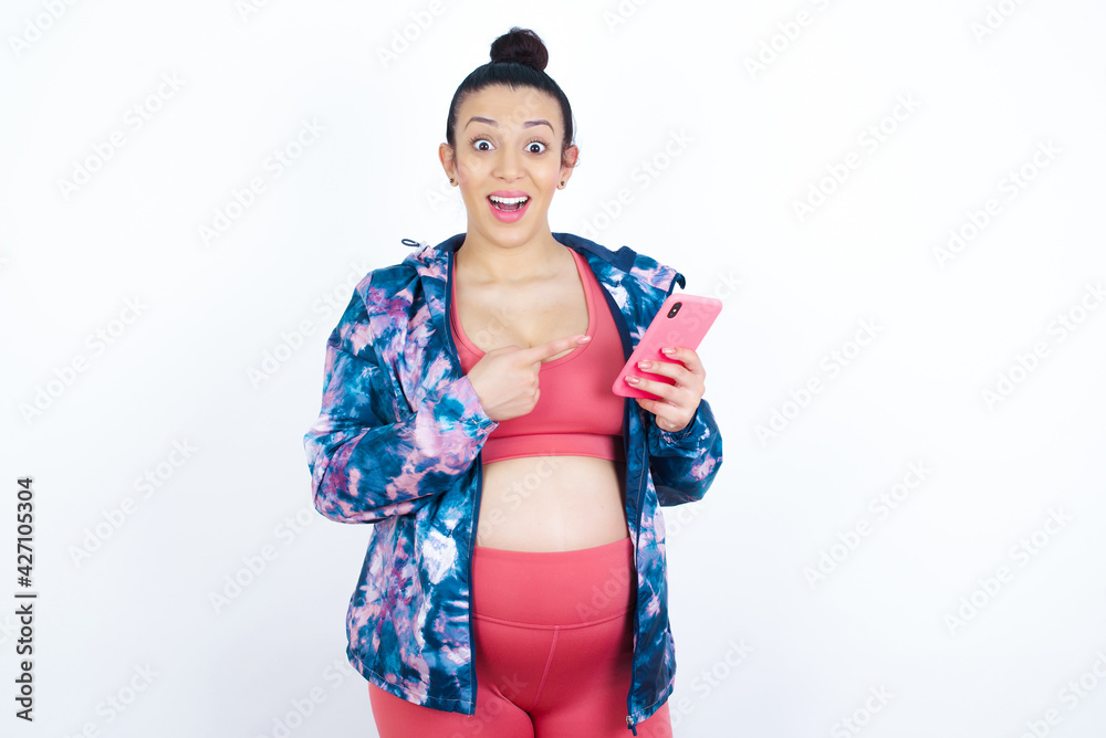 Portrait cute astonished young beautiful Arab pregnant woman in sports clothes against white wall impressed unbelievable unexpected incredible notification advice Portrait cute astonished young beautiful Arab pregnant woman in sports clothes against white wall impressed unbelievable unexpected incredible notification advice