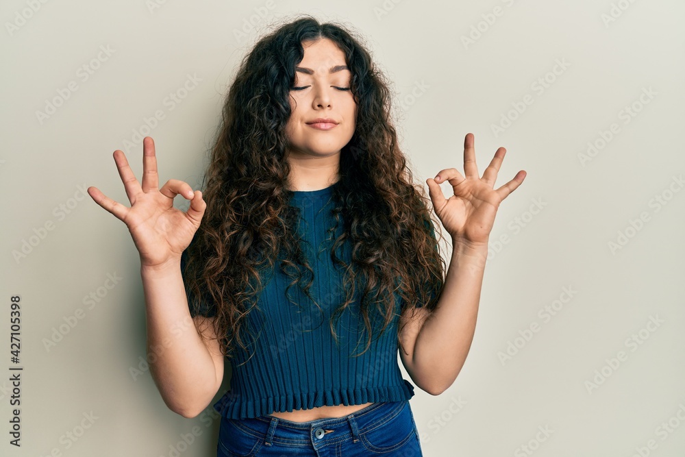 Young brunette woman with curly hair wearing casual clothes relax and smiling with eyes closed doing meditation gesture with fingers. yoga concept. Young brunette woman with curly hair wearing casual clothes relax and smiling with eyes closed doing meditation gesture with fingers. yoga concept.