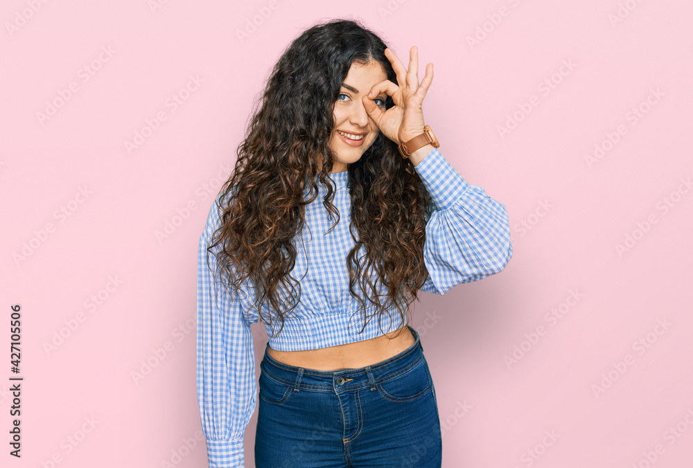 Young hispanic girl wearing casual clothes doing ok gesture with hand smiling, eye looking through fingers with happy face. Young hispanic girl wearing casual clothes doing ok gesture with hand smiling, eye looking through fingers with happy face.