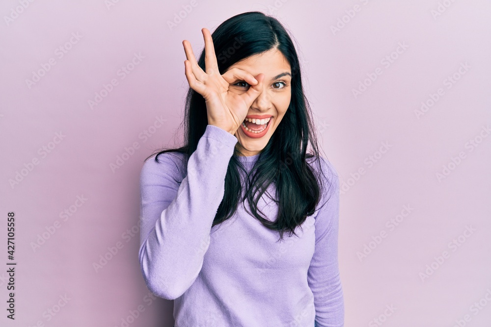 Young hispanic woman wearing casual clothes doing ok gesture with hand smiling, eye looking through fingers with happy face. Young hispanic woman wearing casual clothes doing ok gesture with hand smiling, eye looking through fingers with happy face.