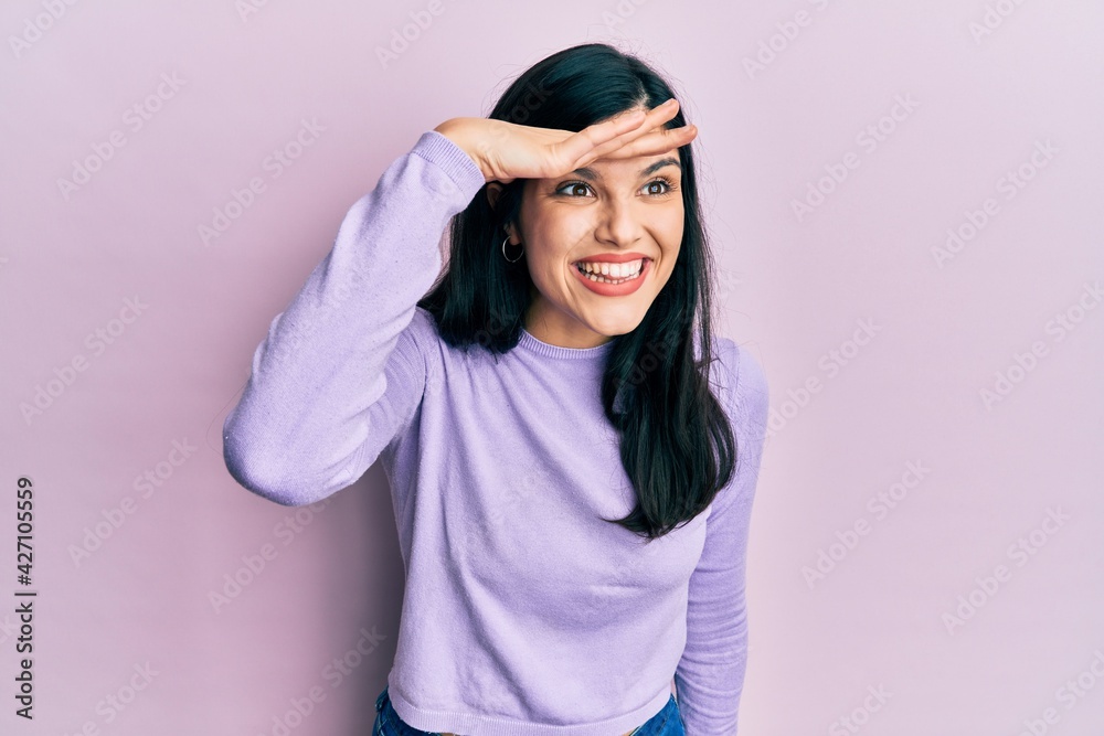 Young hispanic woman wearing casual clothes very happy and smiling looking far away with hand over head. searching concept. Young hispanic woman wearing casual clothes very happy and smiling looking far away with hand over head. searching concept.
