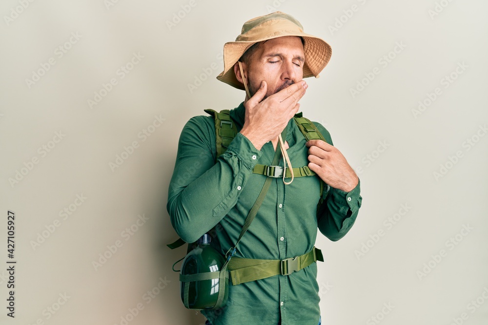 Handsome man with beard wearing explorer hat and backpack bored yawning tired covering mouth with hand. restless and sleepiness. Handsome man with beard wearing explorer hat and backpack bored yawning tired covering mouth with hand. restless and sleepiness.