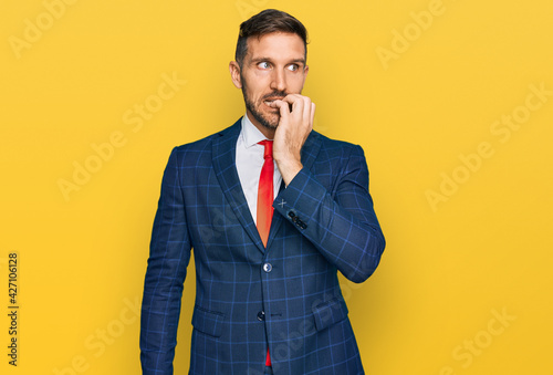 Handsome man with beard wearing business suit and tie looking stressed and nervous with hands on mouth biting nails. anxiety problem.