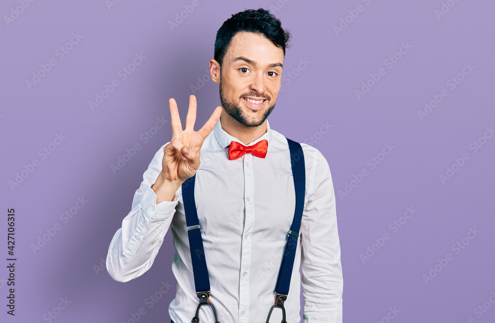 Hispanic man with beard wearing hipster look with bow tie and suspenders showing and pointing up with fingers number three while smiling confident and happy. Hispanic man with beard wearing hipster look with bow tie and suspenders showing and pointing up with fingers number three while smiling confident and happy.