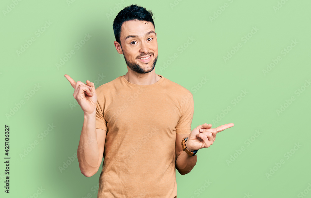 Hispanic man with beard wearing casual t shirt smiling confident pointing with fingers to different directions. copy space for advertisement Hispanic man with beard wearing casual t shirt smiling confident pointing with fingers to different directions. copy space for advertisement