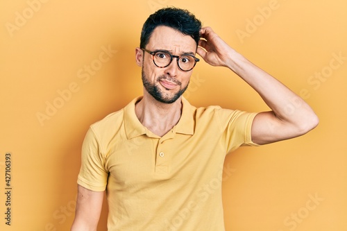 Young hispanic man wearing casual clothes and glasses confuse and wonder about question. uncertain with doubt, thinking with hand on head. pensive concept.