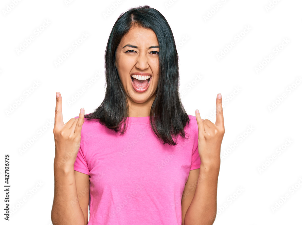 Beautiful asian young woman wearing casual pink t shirt shouting with crazy expression doing rock symbol with hands up. music star. heavy concept. Beautiful asian young woman wearing casual pink t shirt shouting with crazy expression doing rock symbol with hands up. music star. heavy concept.
