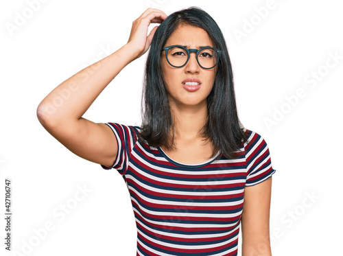 Beautiful asian young woman wearing casual clothes and glasses confuse and wonder about question. uncertain with doubt  thinking with hand on head. pensive concept.