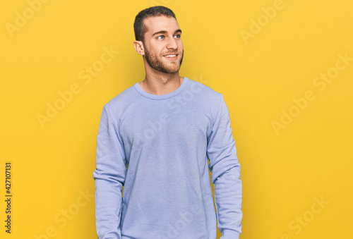 Young caucasian man wearing casual clothes looking away to side with smile on face, natural expression. laughing confident.