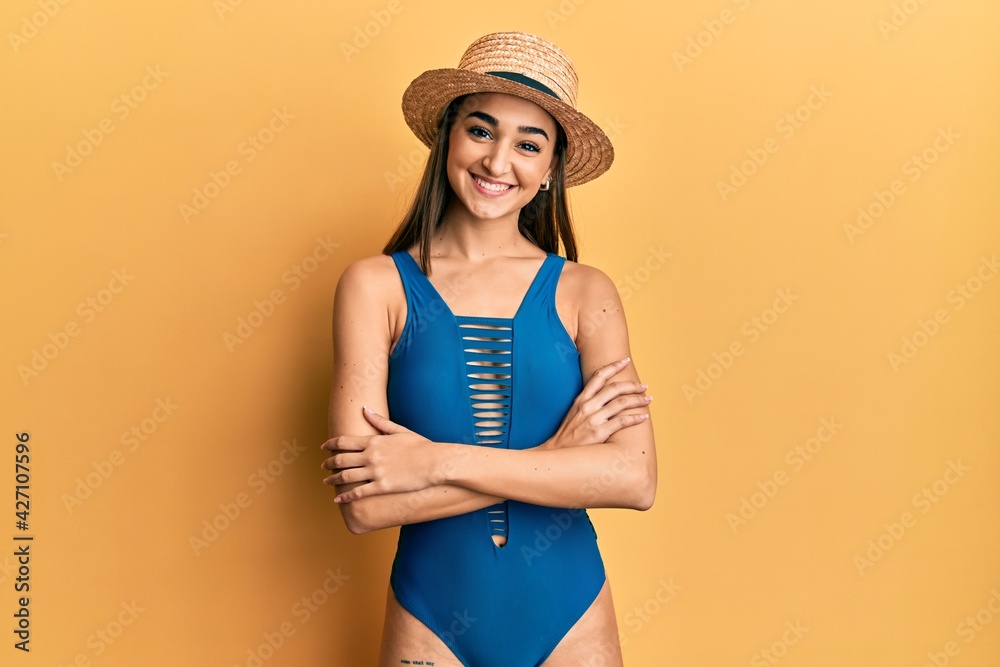 Young brunette girl wearing swimsuit and summer hat happy face smiling with crossed arms looking at the camera. positive person. Young brunette girl wearing swimsuit and summer hat happy face smiling with crossed arms looking at the camera. positive person.