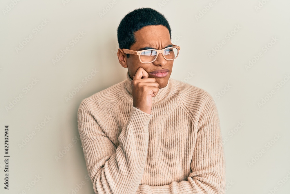 Fototapeta premium Young handsome hispanic man wearing turtleneck neck sweater and glasses thinking concentrated about doubt with finger on chin and looking up wondering