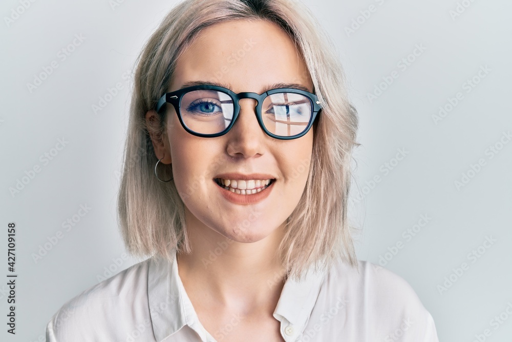 Young blonde girl wearing casual clothes and glasses looking positive and happy standing and smiling with a confident smile showing teeth