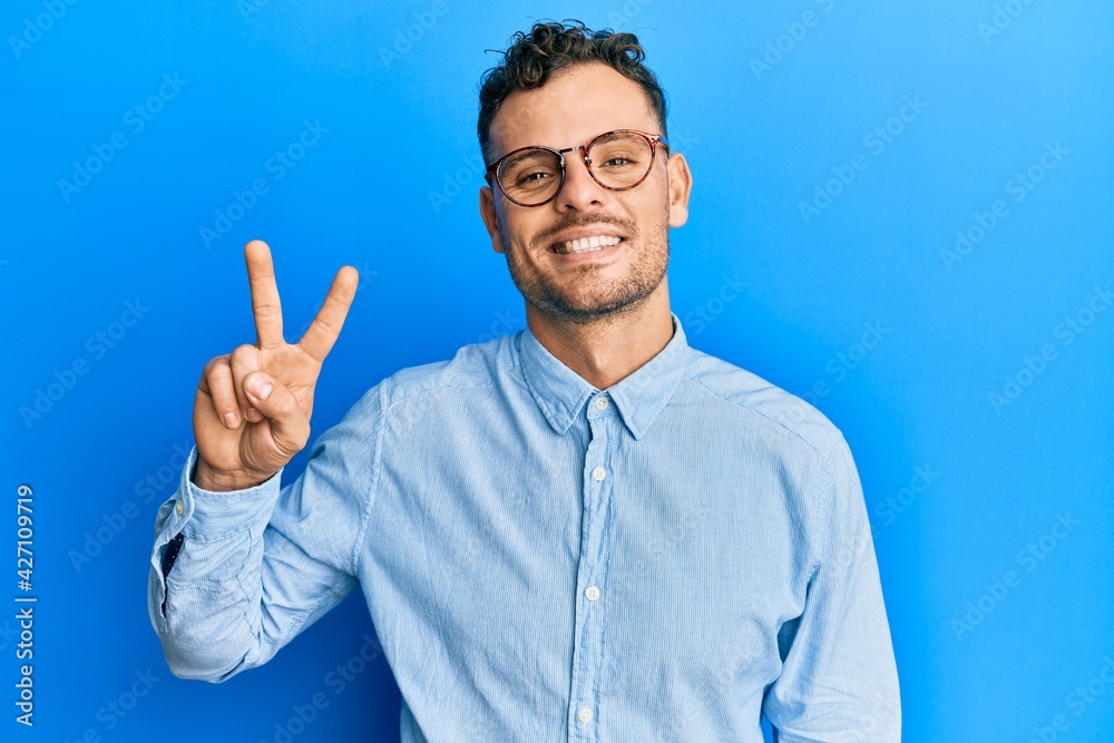 Young hispanic man wearing casual clothes and glasses smiling looking to the camera showing fingers doing victory sign. number two. Young hispanic man wearing casual clothes and glasses smiling looking to the camera showing fingers doing victory sign. number two.