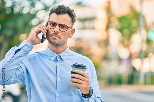 Young hispanic businessman with serious expression talking on the smartphone and drinking coffee at the city.