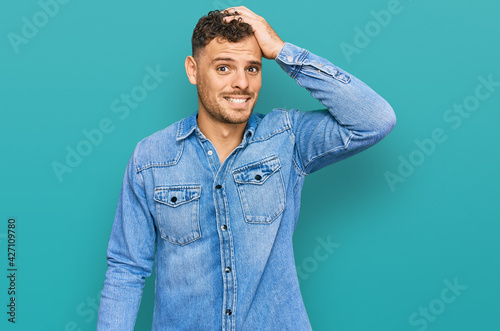 Young hispanic man wearing casual denim jacket confuse and wonder about question. uncertain with doubt, thinking with hand on head. pensive concept.