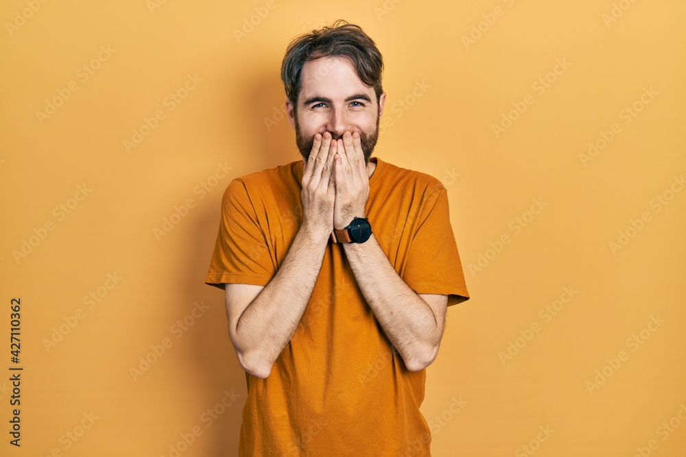 Caucasian man with beard wearing casual yellow t shirt laughing and embarrassed giggle covering mouth with hands, gossip and scandal concept Caucasian man with beard wearing casual yellow t shirt laughing and embarrassed giggle covering mouth with hands, gossip and scandal concept