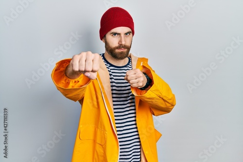 Caucasian man with beard wearing yellow raincoat punching fist to fight, aggressive and angry attack, threat and violence