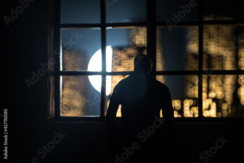 The silhouette of a man with arms crossed in front of a window with a view over a city lit in the night.