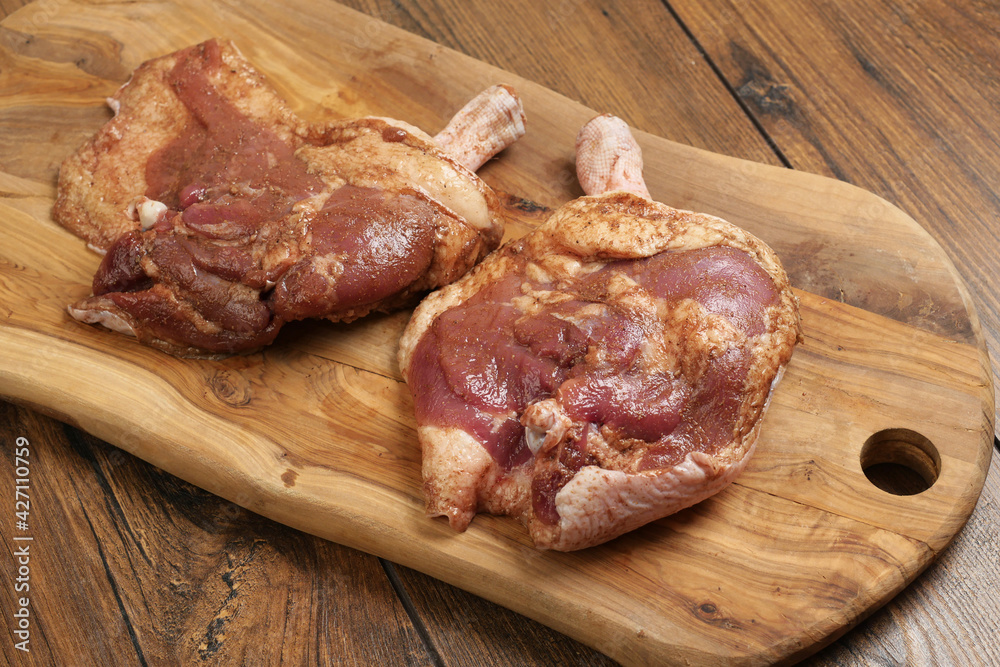 Two fresh uncooked duck legs on a wooden cutting board and wooden table. Poultry product.