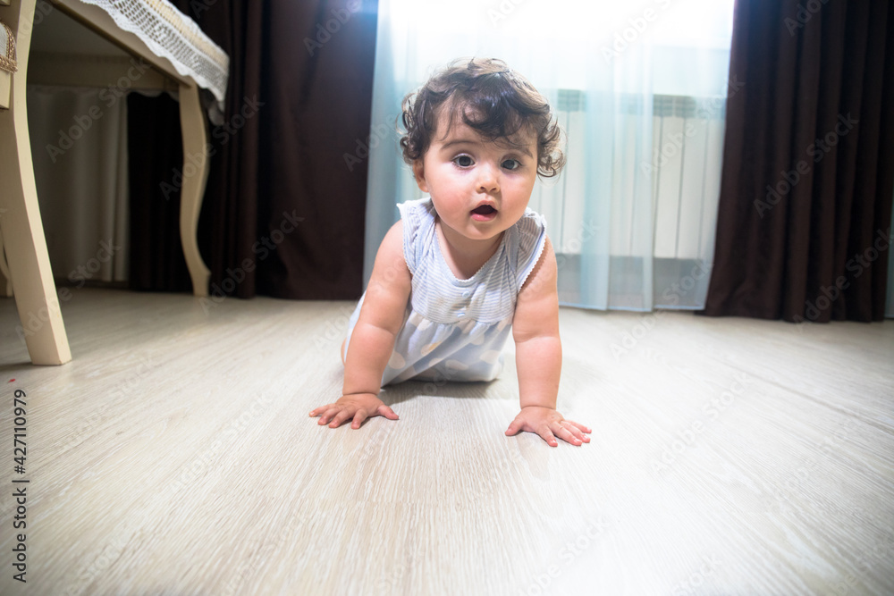 Baby Girl In Summer Dress Sit on wooden floor inside room.
