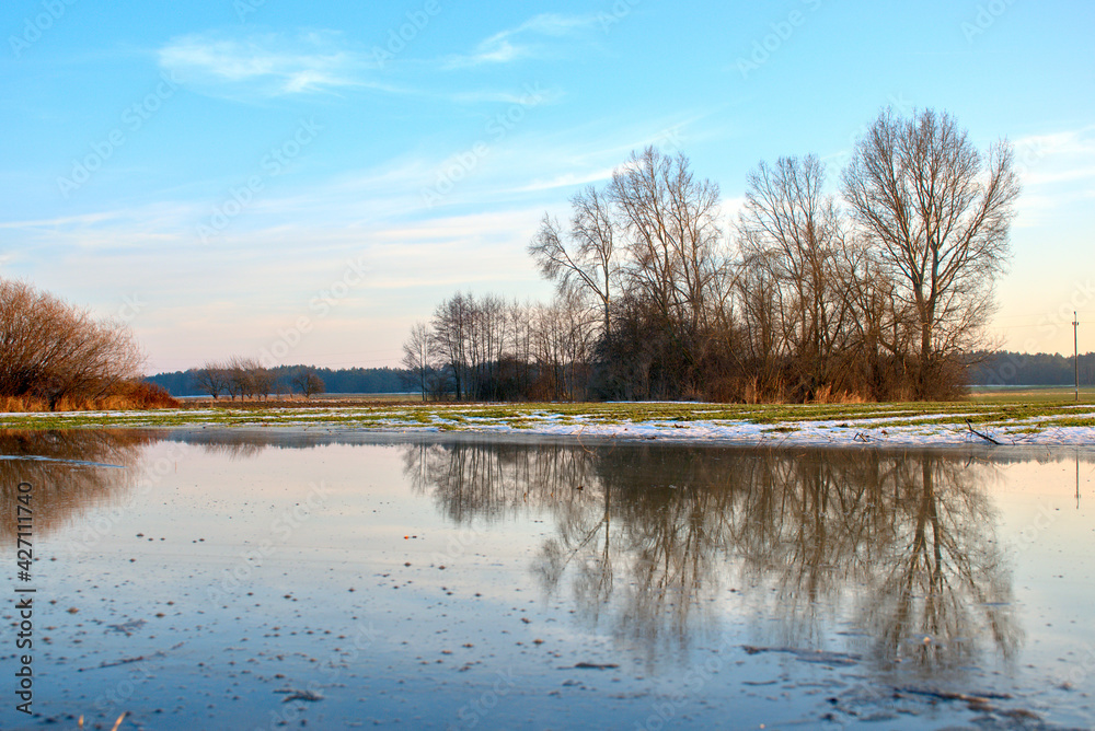 spring thaws on a green field, reflected in water