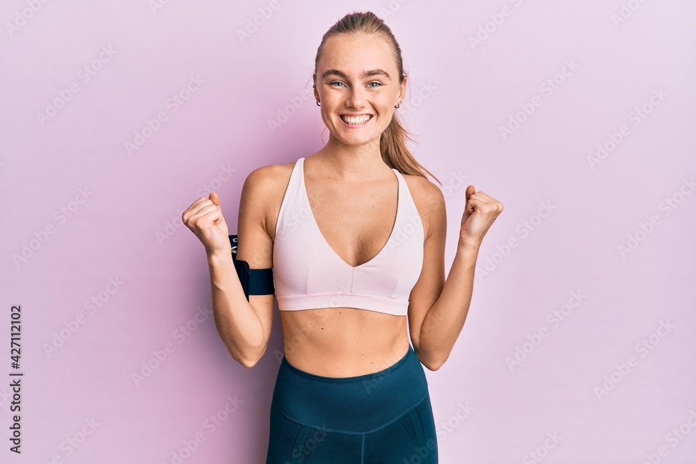 Beautiful blonde woman wearing sportswear and arm band celebrating surprised and amazed for success with arms raised and open eyes. winner concept. Beautiful blonde woman wearing sportswear and arm band celebrating surprised and amazed for success with arms raised and open eyes. winner concept.