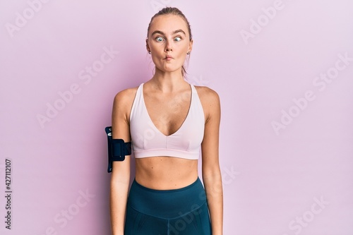 Beautiful blonde woman wearing sportswear and arm band making fish face with lips, crazy and comical gesture. funny expression. © Krakenimages.com