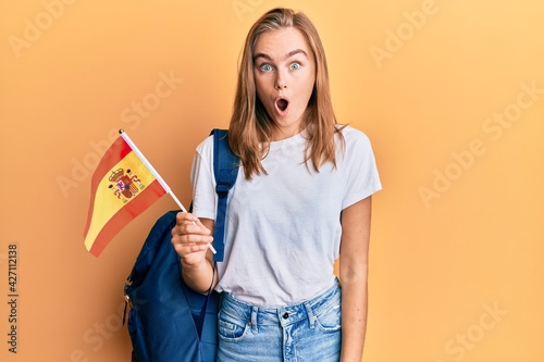 Beautiful blonde woman exchange student holding spanish flag scared and amazed with open mouth for surprise  disbelief face