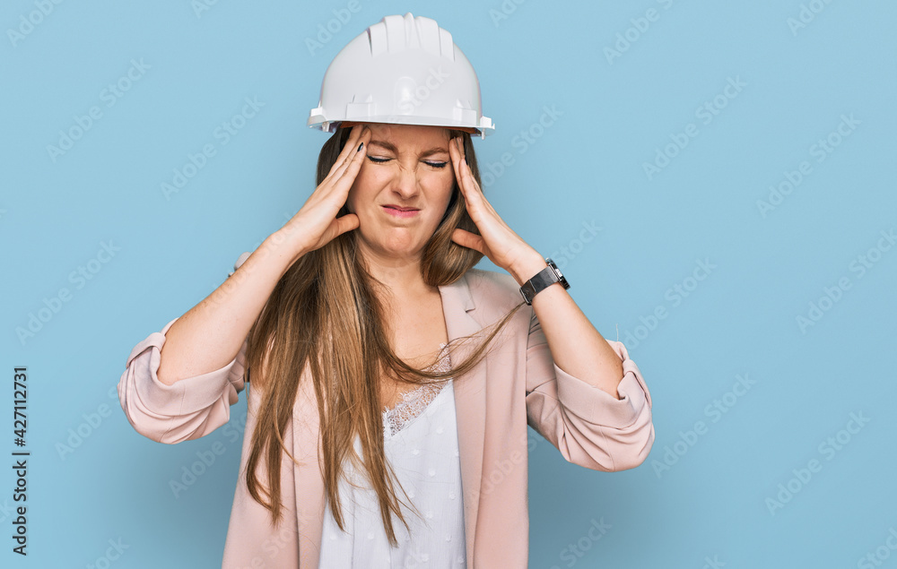 Young blonde woman wearing architect hardhat suffering from headache desperate and stressed because pain and migraine. hands on head. Young blonde woman wearing architect hardhat suffering from headache desperate and stressed because pain and migraine. hands on head.