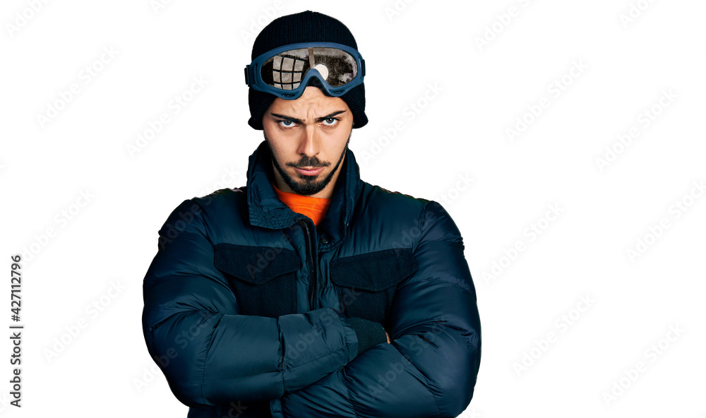 Young hispanic man with beard wearing snow wear and sky glasses skeptic and nervous, disapproving expression on face with crossed arms. negative person. Young hispanic man with beard wearing snow wear and sky glasses skeptic and nervous, disapproving expression on face with crossed arms. negative person.