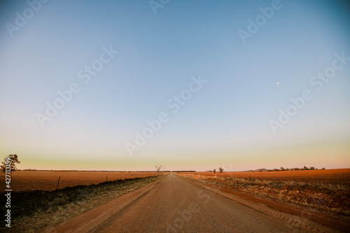 Dirt country road at dusk with moon visible in the clear sky
