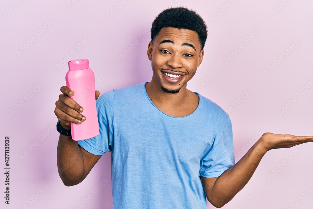 Young african american man holding shampoo bottle celebrating victory with happy smile and winner expression with raised hands Young african american man holding shampoo bottle celebrating victory with happy smile and winner expression with raised hands