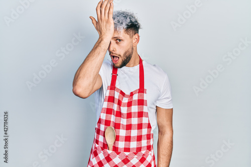 Canvastavla Young hispanic man with modern dyed hair wearing apron surprised with hand on head for mistake, remember error