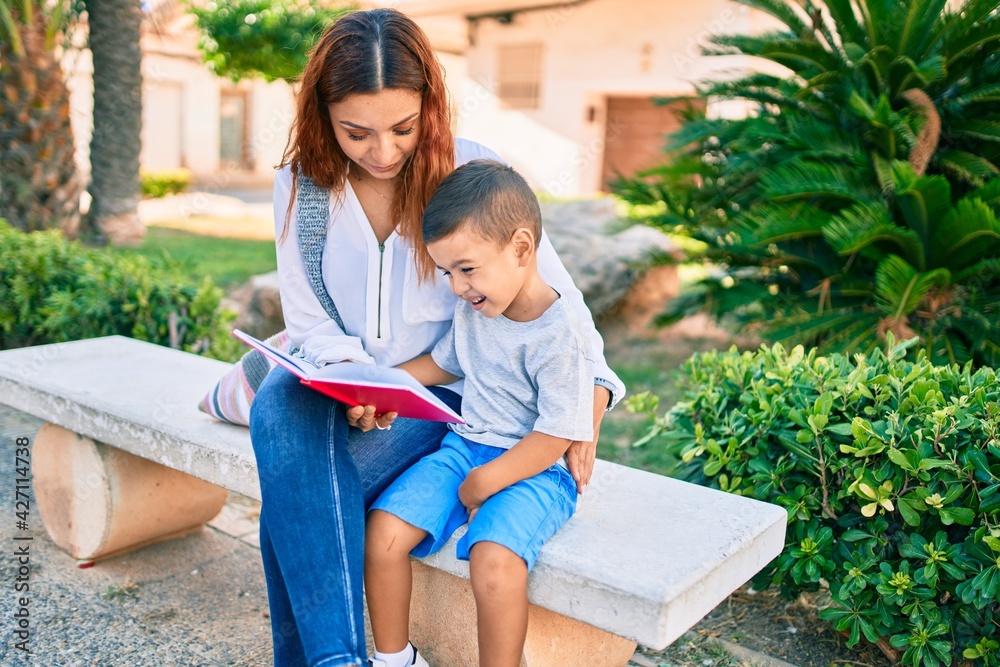 Adorable latin mother and son sitting on the bench and reading book at the park. Adorable latin mother and son sitting on the bench and reading book at the park.