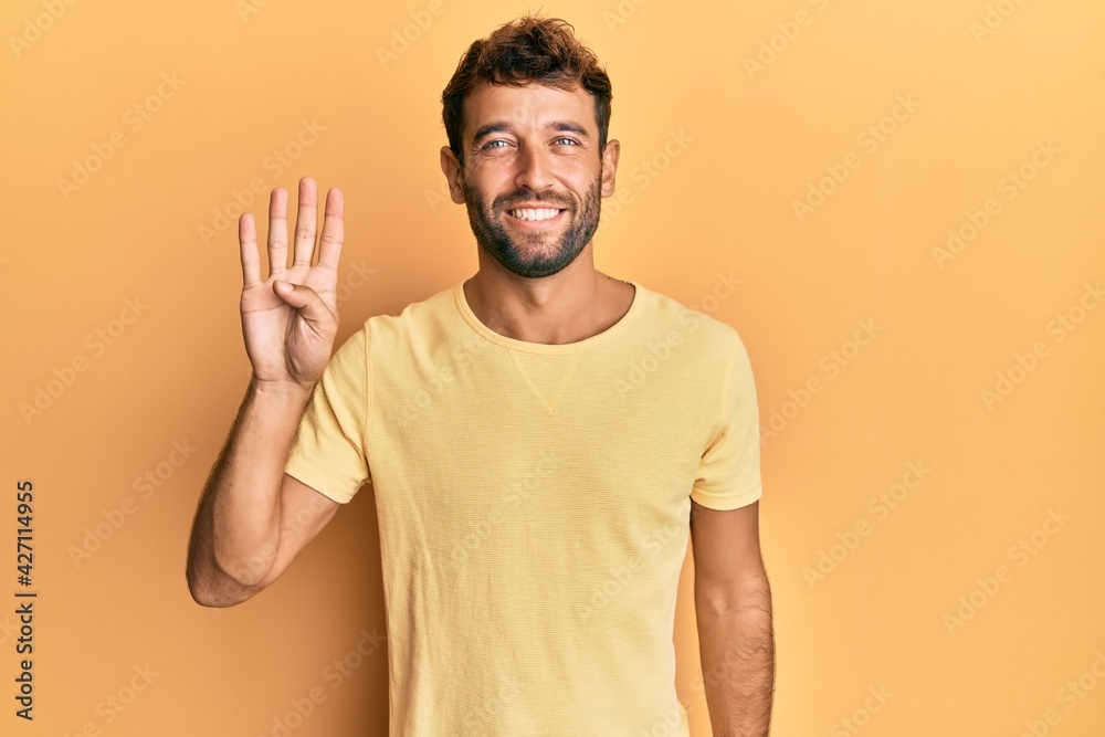 Handsome man with beard wearing casual yellow tshirt over yellow background showing and pointing up with fingers number four while smiling confident and happy. Handsome man with beard wearing casual yellow tshirt over yellow background showing and pointing up with fingers number four while smiling confident and happy.