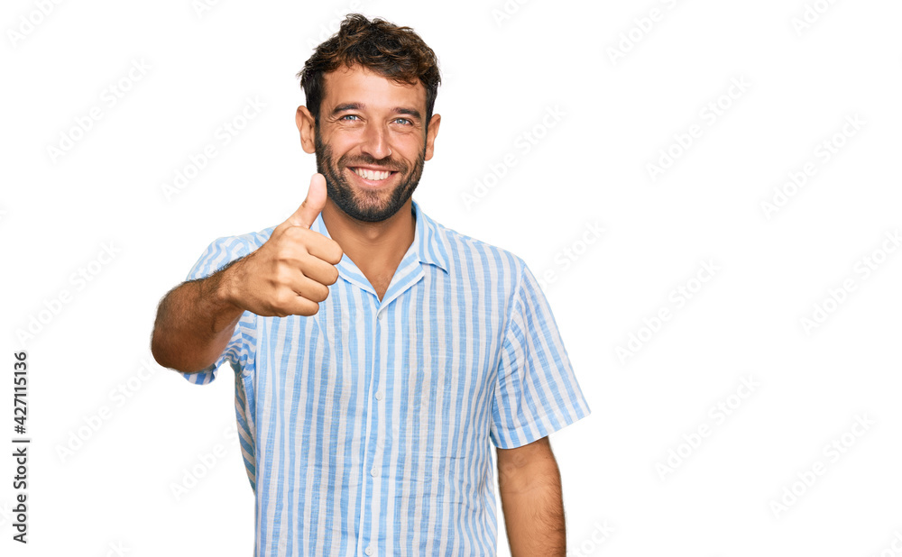 Handsome young man with beard wearing casual fresh shirt doing happy thumbs up gesture with hand. approving expression looking at the camera showing success. Handsome young man with beard wearing casual fresh shirt doing happy thumbs up gesture with hand. approving expression looking at the camera showing success.