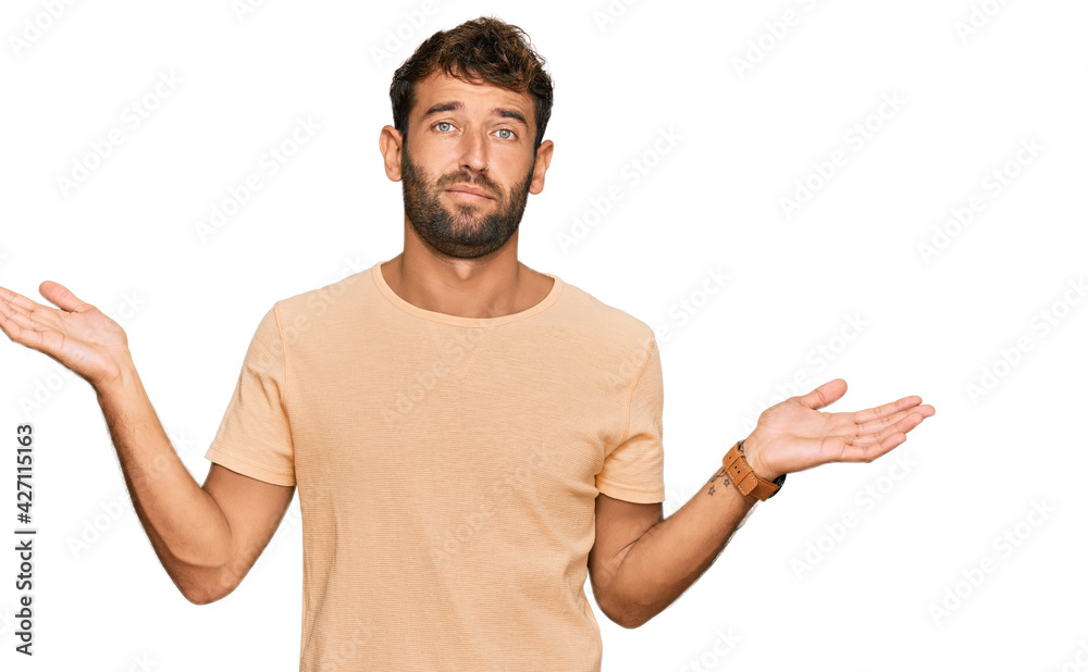 Handsome young man with beard wearing casual tshirt clueless and confused expression with arms and hands raised. doubt concept. Handsome young man with beard wearing casual tshirt clueless and confused expression with arms and hands raised. doubt concept.