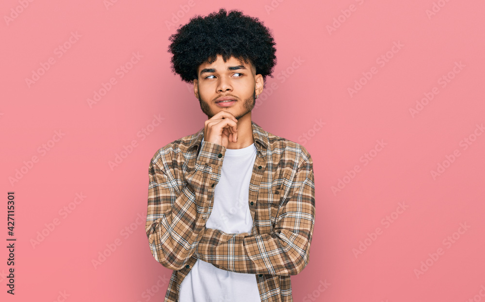 Young african american man with afro hair wearing casual clothes with hand on chin thinking about question, pensive expression. smiling with thoughtful face. doubt concept. Young african american man with afro hair wearing casual clothes with hand on chin thinking about question, pensive expression. smiling with thoughtful face. doubt concept.