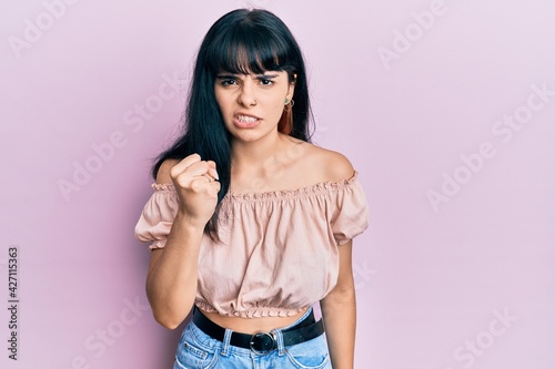 Young hispanic girl wearing casual clothes angry and mad raising fist frustrated and furious while shouting with anger. rage and aggressive concept.