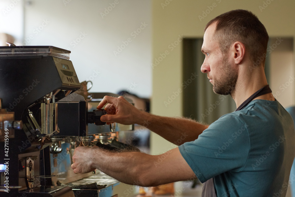 Side view portrait of male barista making fresh coffee in cafe and operating coffee machine