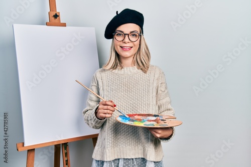 Beautiful caucasian woman drawing with palette on easel stand smiling with a happy and cool smile on face. showing teeth.