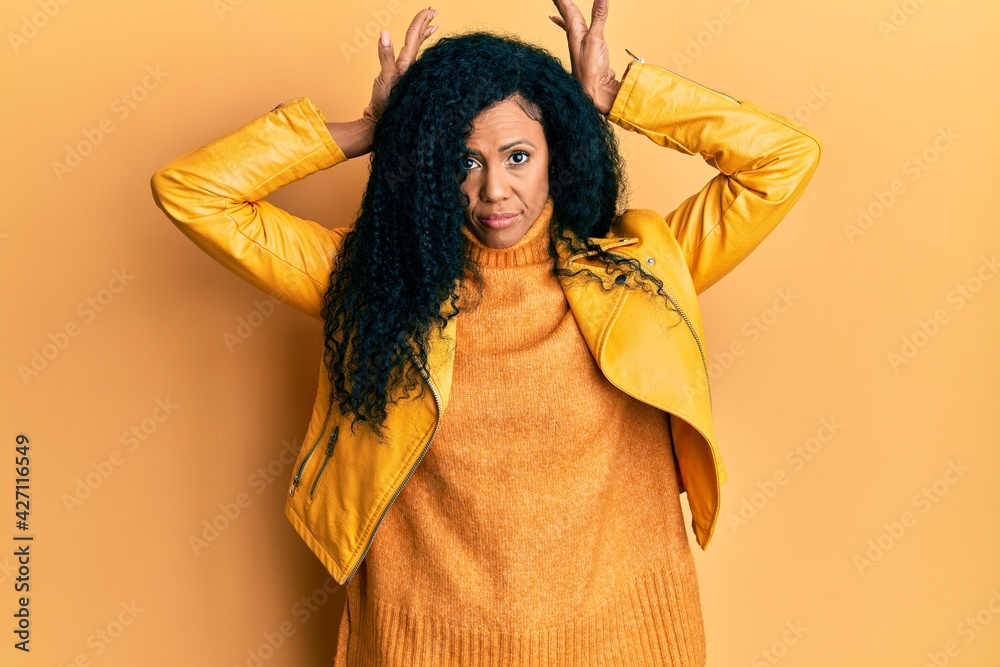 Middle age african american woman wearing wool winter sweater and leather jacket doing bunny ears gesture with hands palms looking cynical and skeptical. easter rabbit concept. Middle age african american woman wearing wool winter sweater and leather jacket doing bunny ears gesture with hands palms looking cynical and skeptical. easter rabbit concept.