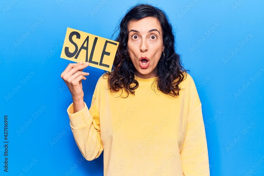 Young beautiful hispanic woman holding sale poster scared and amazed with open mouth for surprise, disbelief face Young beautiful hispanic woman holding sale poster scared and amazed with open mouth for surprise, disbelief face