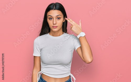 Foto Young hispanic girl wearing casual white t shirt shooting and killing oneself pointing hand and fingers to head like gun, suicide gesture