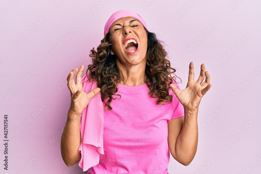 Middle age hispanic woman wearing breast cancer support pink scarf crazy and mad shouting and yelling with aggressive expression and arms raised. frustration concept. Middle age hispanic woman wearing breast cancer support pink scarf crazy and mad shouting and yelling with aggressive expression and arms raised. frustration concept.