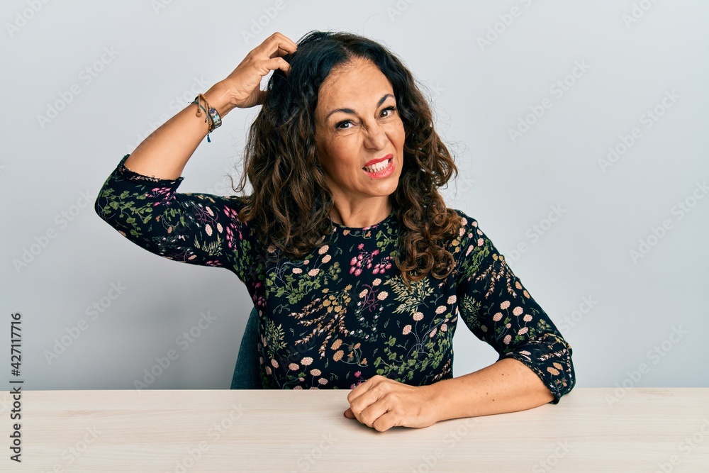 Beautiful middle age woman wearing casual clothes sitting on the table confuse and wonder about question. uncertain with doubt, thinking with hand on head. pensive concept. Beautiful middle age woman wearing casual clothes sitting on the table confuse and wonder about question. uncertain with doubt, thinking with hand on head. pensive concept.