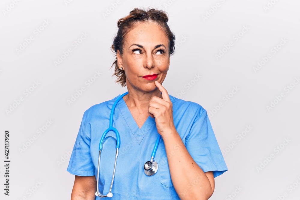 Middle age brunette nurse woman wearing uniform and stethoscope over white background thinking concentrated about doubt with finger on chin and looking up wondering Middle age brunette nurse woman wearing uniform and stethoscope over white background thinking concentrated about doubt with finger on chin and looking up wondering
